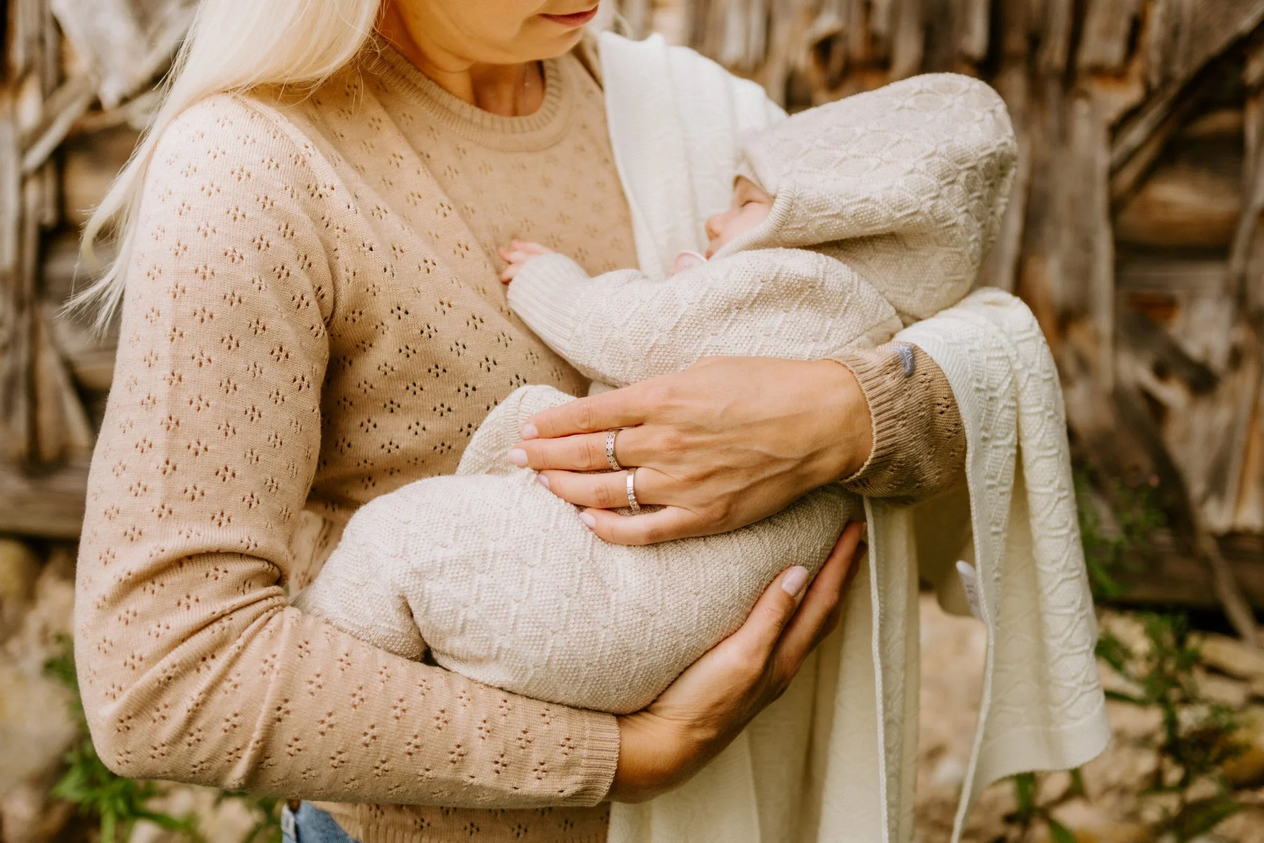 Mother holding baby in cream knitted romper and hooded blanket with geometric pattern