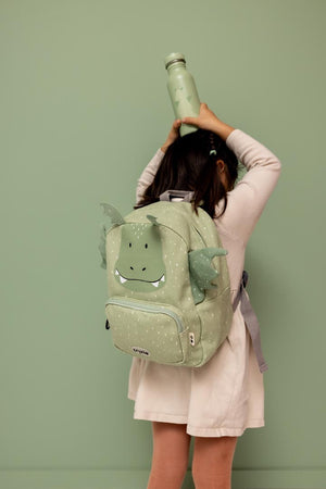Child wearing the Trixie Mr. Dragon backpack while holding a matching green bottle above their head