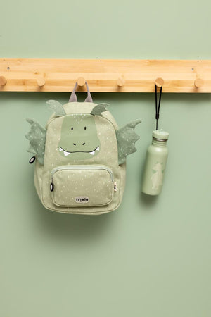Trixie Mr. Dragon backpack hanging from a wooden peg beside a matching green drinking bottle