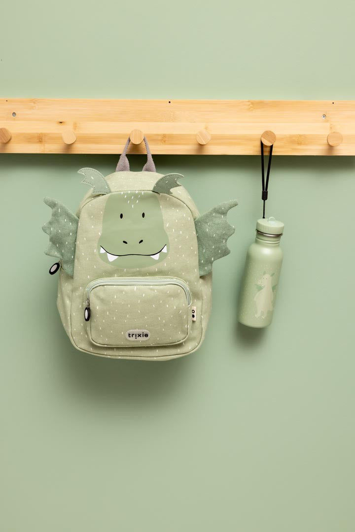 Trixie Mr. Dragon backpack hanging from a wooden peg beside a matching green drinking bottle