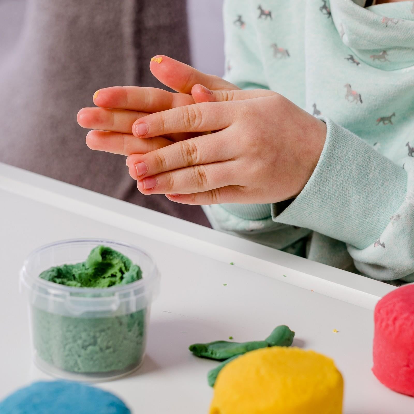 Close-up of child’s hands rolling Neogrün modelling clay beside green, yellow, blue and red colours