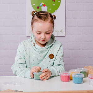 Child opening a green Neogrün Easy Clay pot with four colourful modelling clay pots on the table