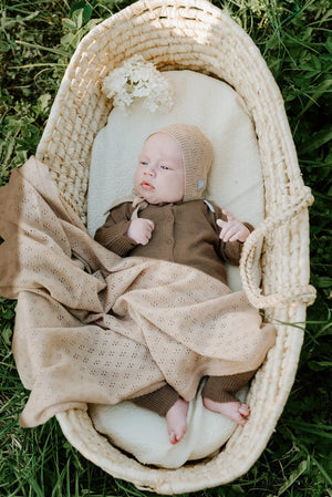 Nouveau-né dans un couffin en osier naturel avec tricot beige et couverture à œillets en extérieur
