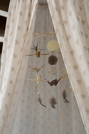 Origami paper crane mobile hanging inside a softly patterned children’s canopy