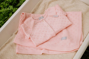 Set gilet et couverture bébé en tricot rose, coton bio, sur literie beige texturée