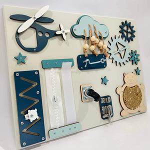 Wooden toddler activity board with airplane, zipper, gears, cloud beads, and teddy bear sequin panel in blue and cream