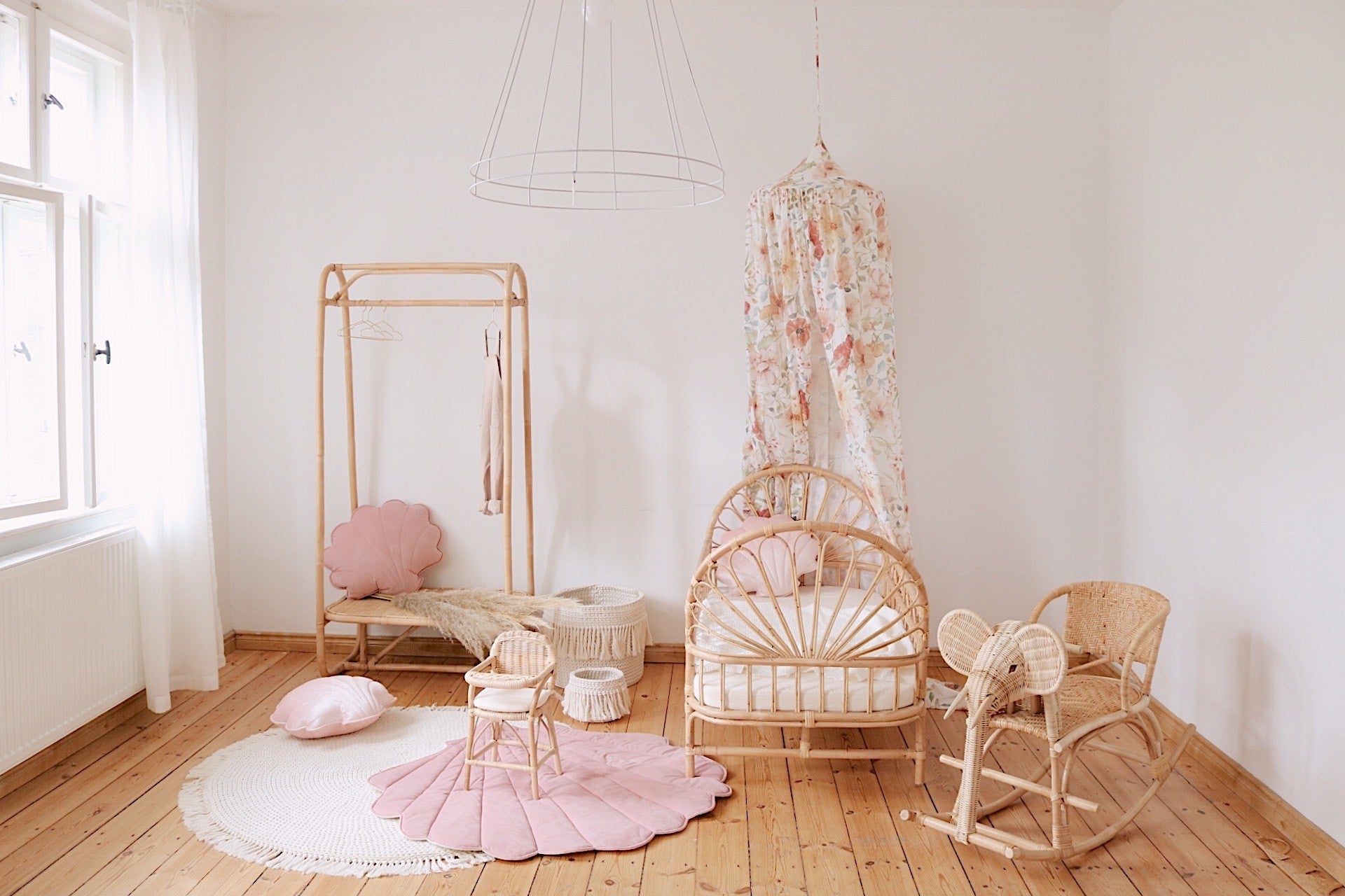 Powder pink shell playmat styled in a bright rattan nursery with a floral canopy and wooden furniture
