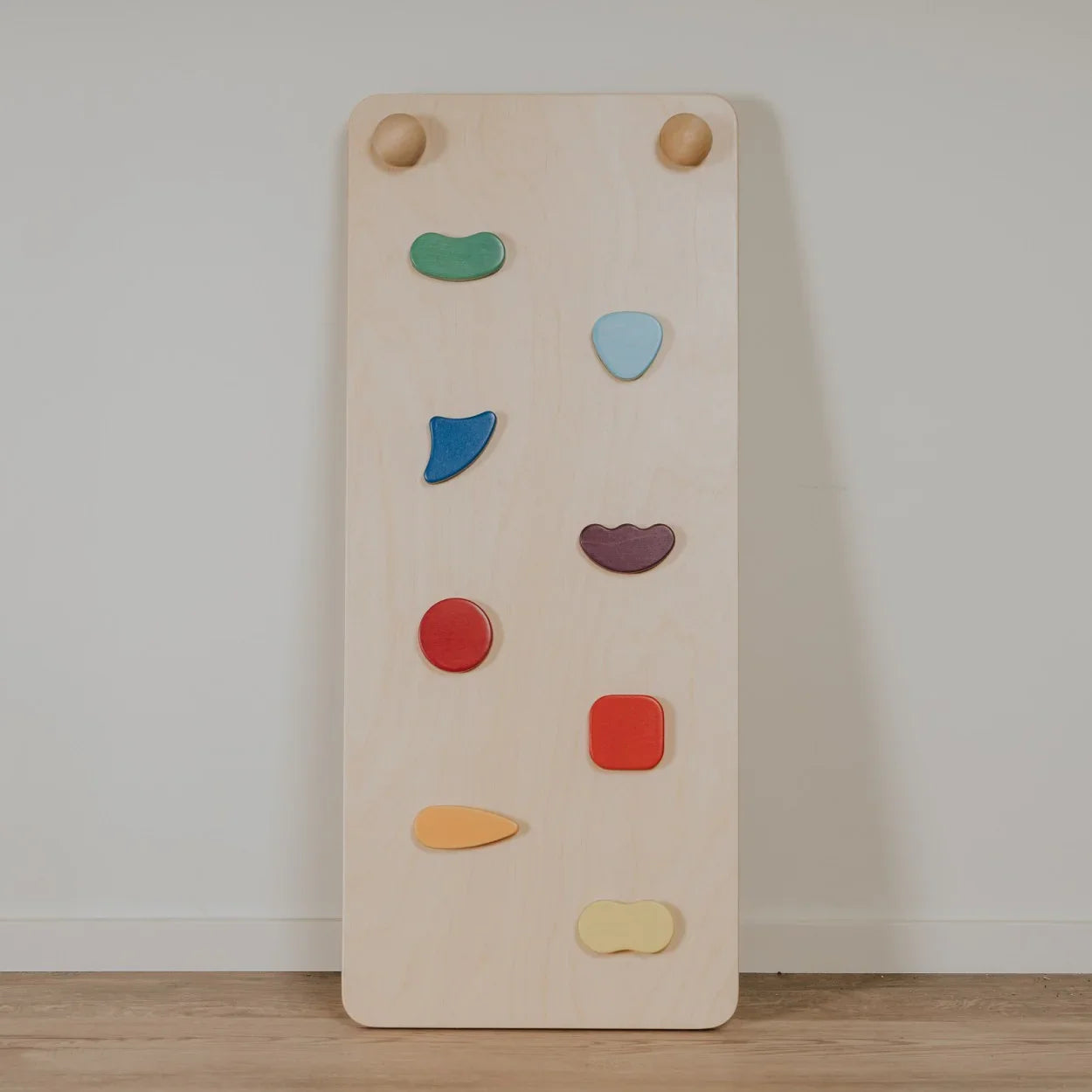 Wooden kids climbing wall with colorful geometric handholds, natural finish, for indoor play and nursery decor