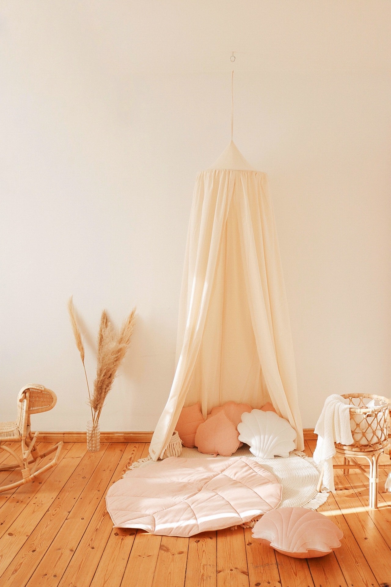 Raw cotton canopy styled with a blush leaf playmat and shell cushions in warm sunlight