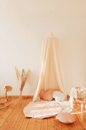 Raw cotton canopy styled with a blush leaf playmat and shell cushions in warm sunlight