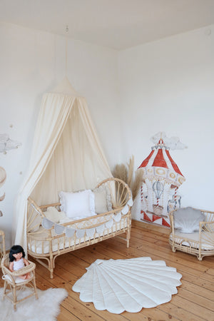 Cream cotton canopy above a rattan child’s bed beside circus wall art and a white shell playmat