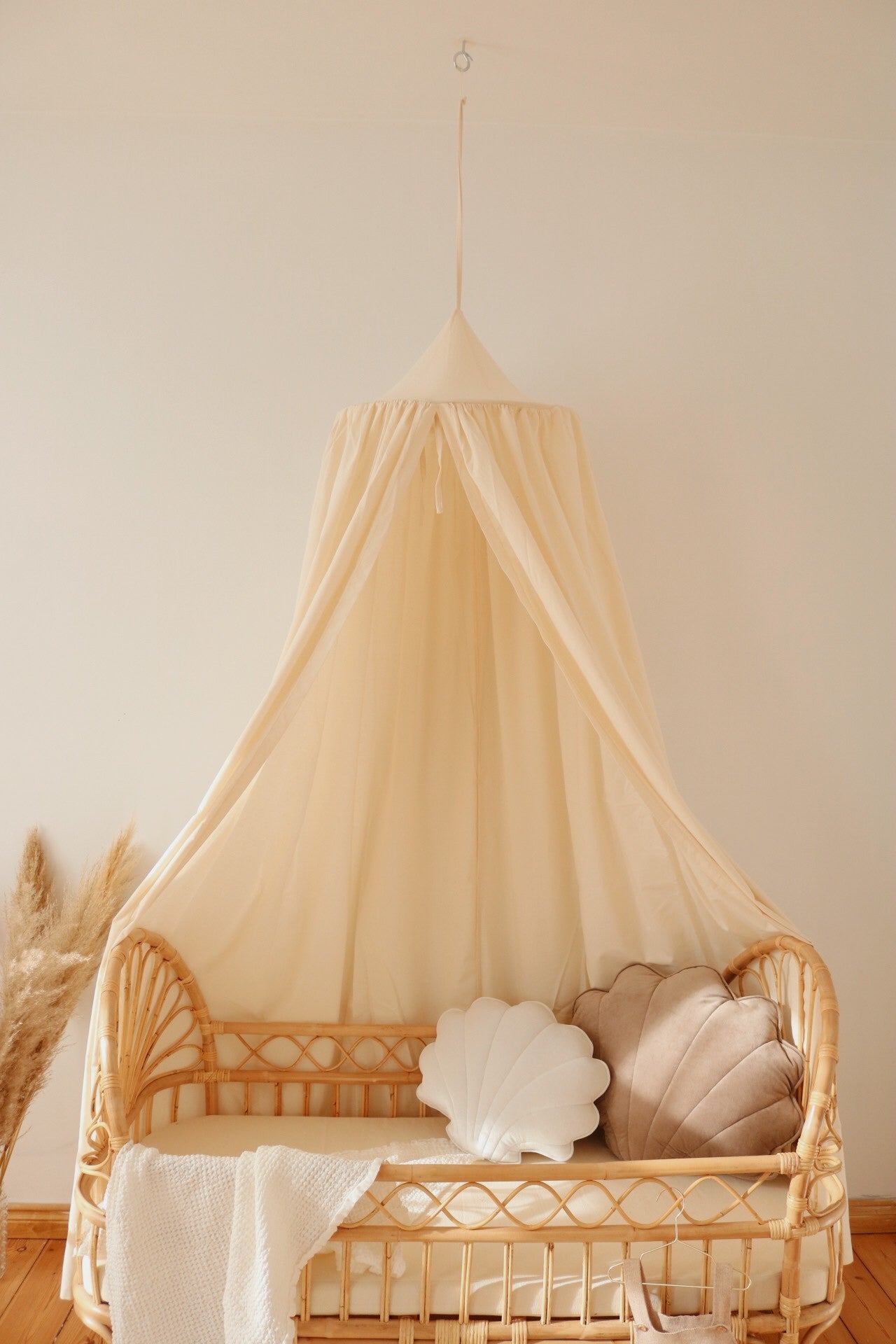 Cream Moi Mili canopy above a rattan bed with neutral shell cushions and a knitted blanket