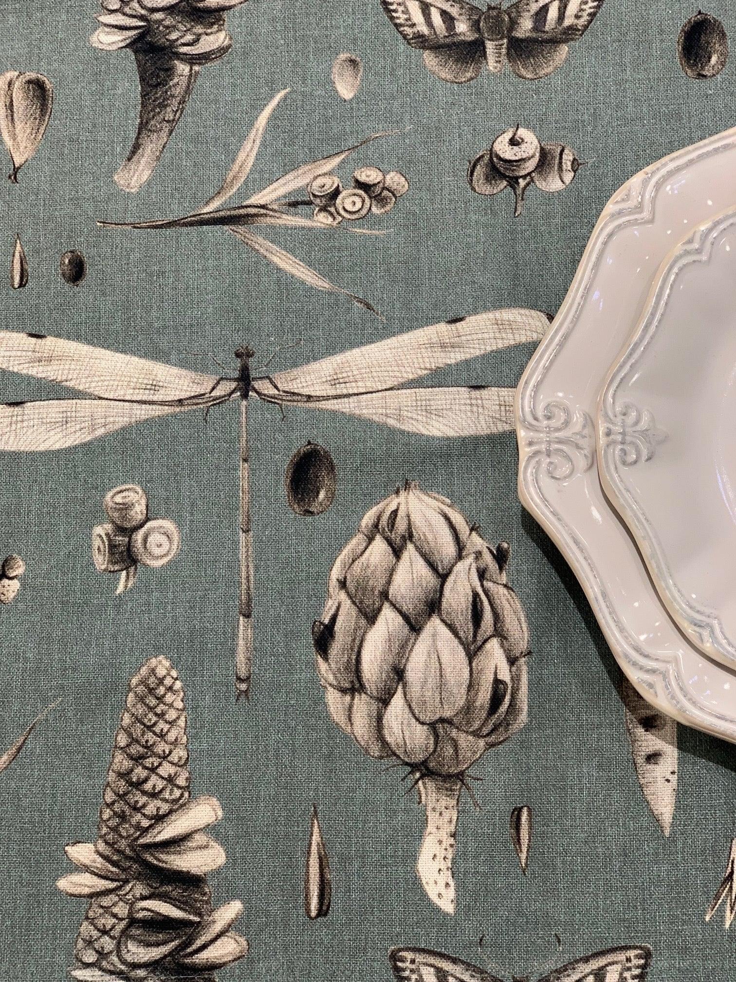 Teal botanical tablecloth with dragonfly, pinecone, and moth print, paired with white ornate ceramic plates