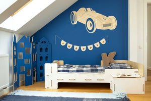 Cama infantil de madera blanca con cajones, ropa de cama de cuadros azules y decoración de pared con paisaje urbano azul.