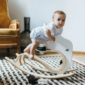 White wooden rocking toy shaped like a swan with natural wood base, baby seated on it in nursery setting