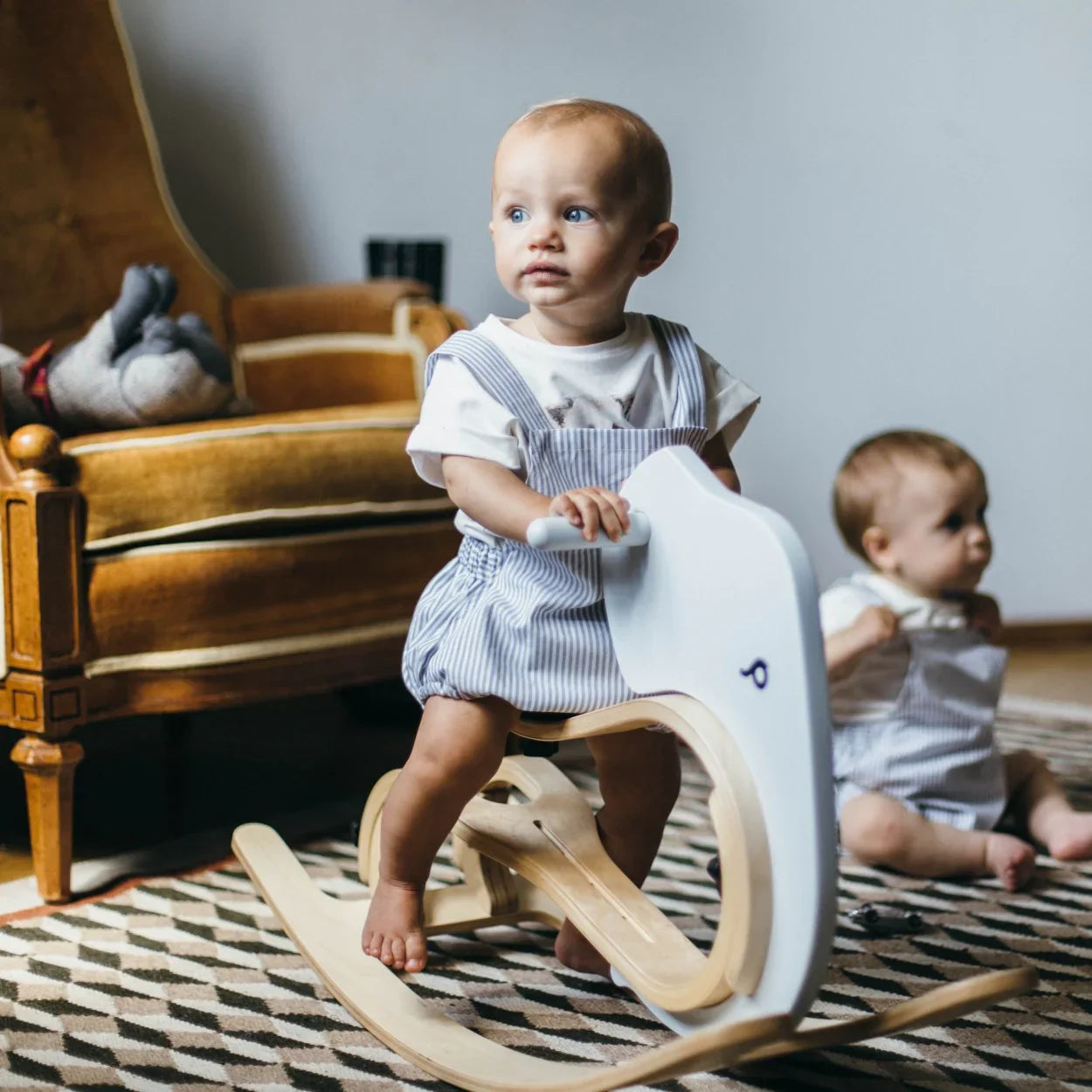 Baby on white and natural wood rocking horse, nursery decor, striped overalls, patterned rug