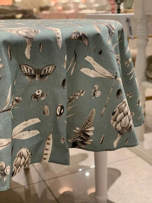 Teal tablecloth with botanical insect print, featuring moths, dragonflies, and seed pods on round table