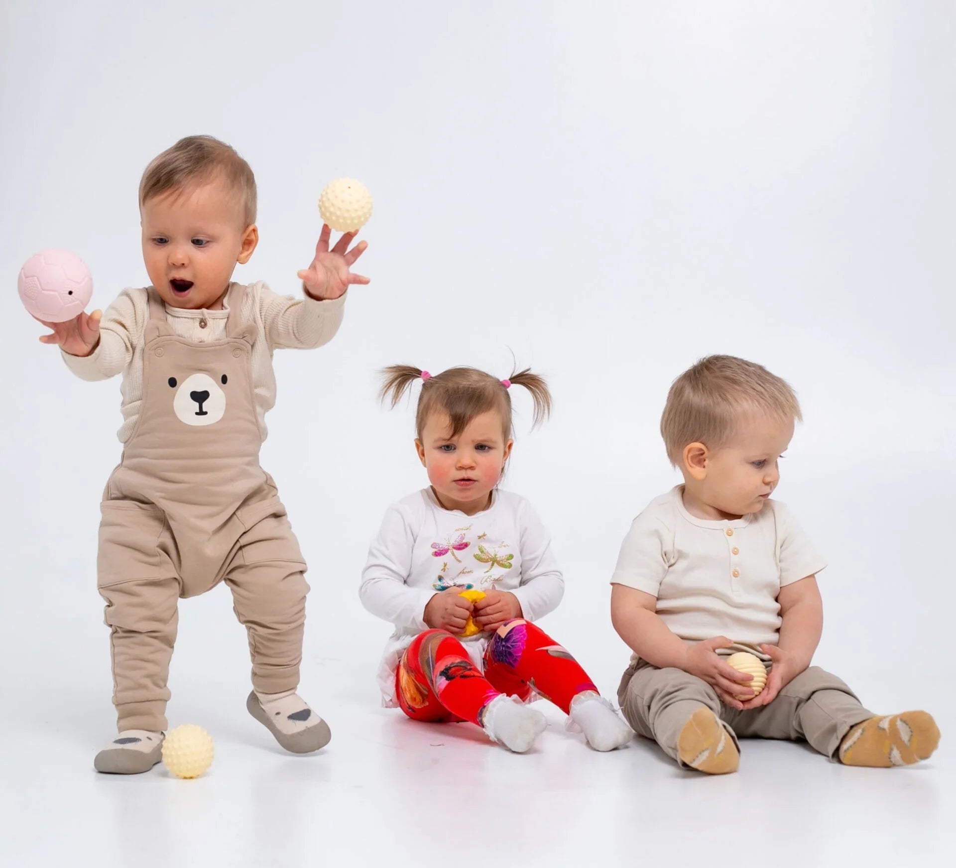 Neonati che giocano con un set di palline sensoriali testurizzate in colori pastello su sfondo bianco