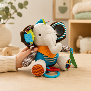 Soft sensory elephant baby toy held on wooden table with mirror, ribbons, textured pieces and grasping rings