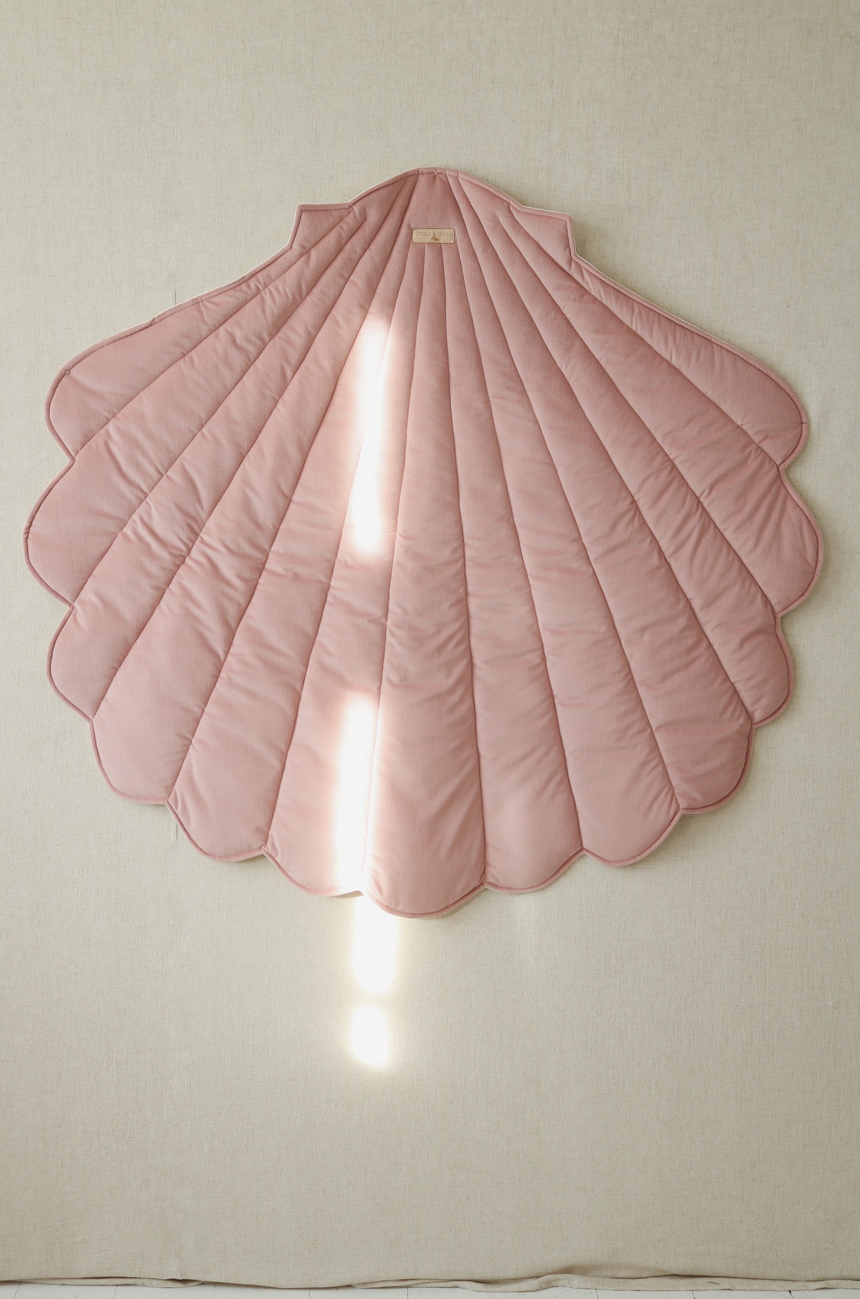 Powder pink shell-shaped textile playmat hanging vertically as children’s room wall décor