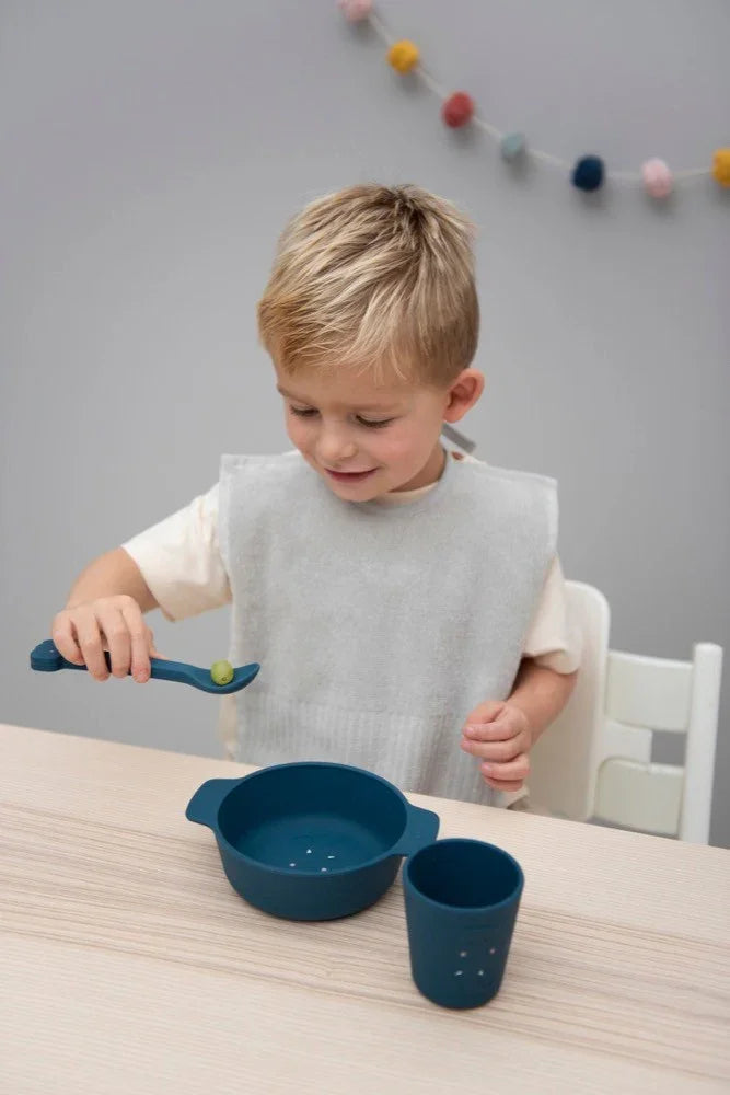 Set bol, gobelet et cuillère en silicone bleu pour enfants sur table en bois, utilisé par un enfant