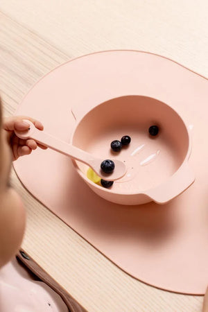 Bol tout-petit en silicone rose avec cuillère assortie, myrtilles à l'intérieur, posé sur une table en bois
