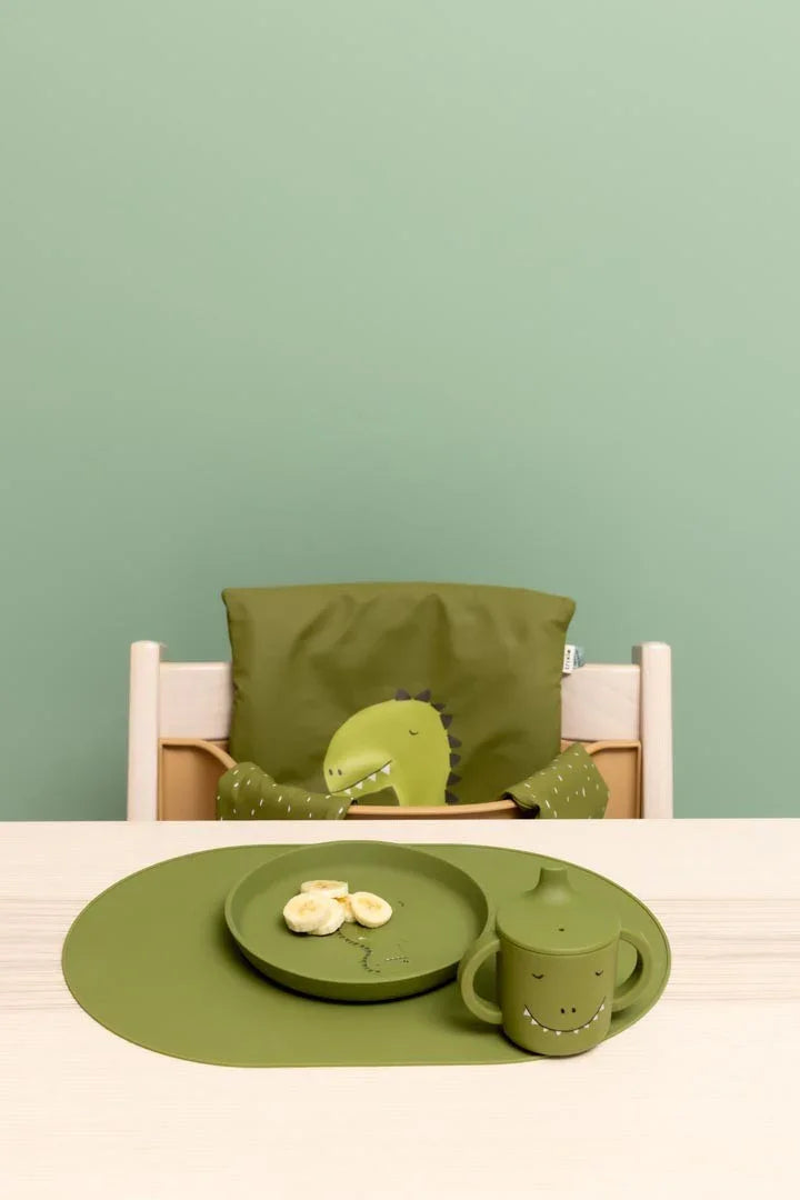 Set de plato y vaso de silicona verde para niños con diseño de dinosaurio sobre un mantel individual