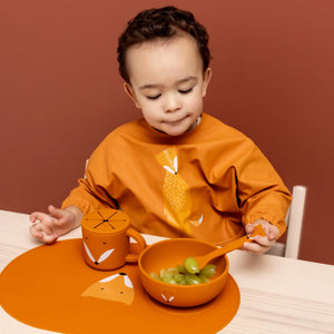 Tout-petit utilisant un set de repas en silicone orange motif renard, incluant assiette, gobelet, cuillère et set de table