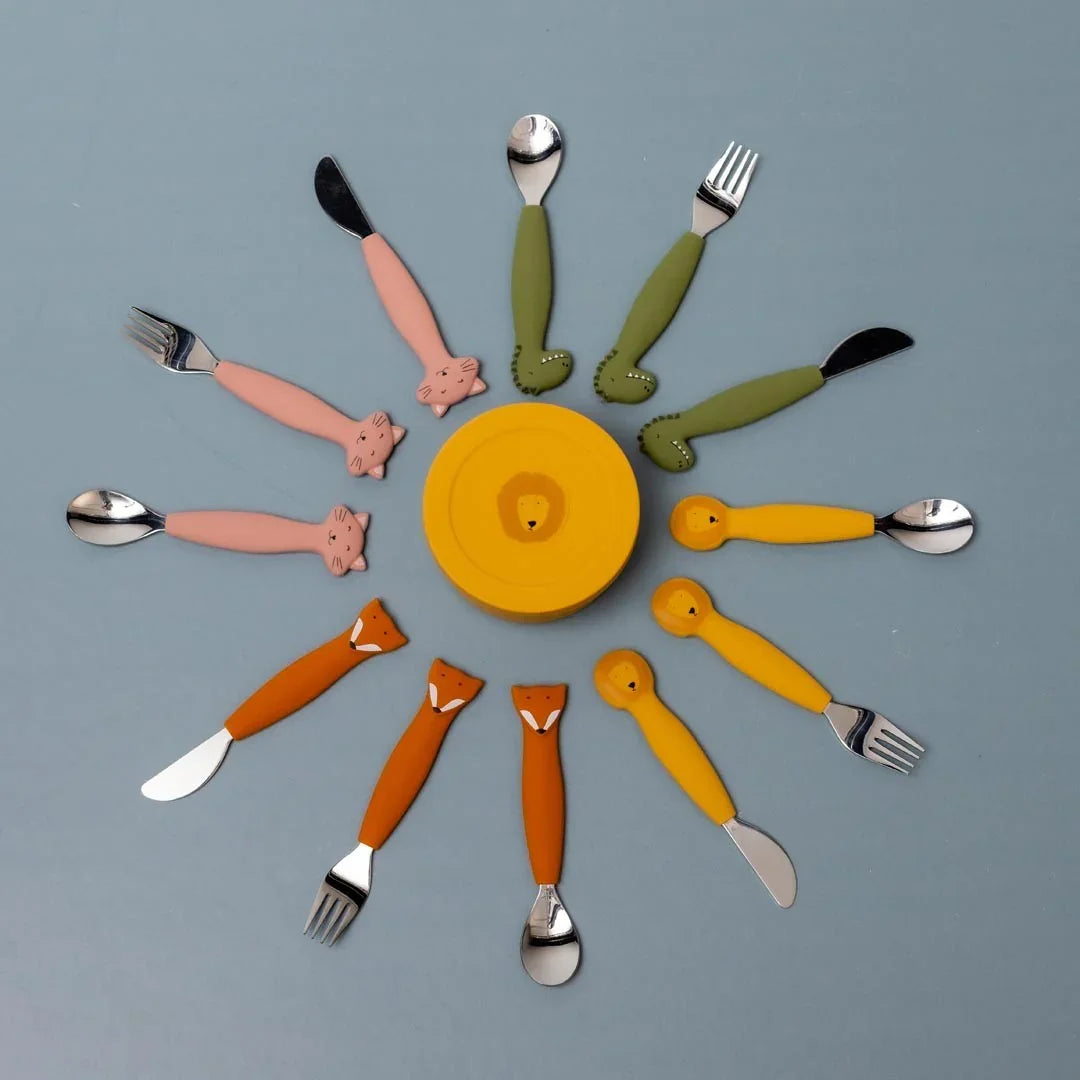 Récipient à goûter en silicone jaune avec couvercle motif lion, entouré de couverts à motifs animaux sur fond bleu