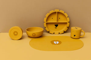 Récipient à goûter en silicone jaune avec couvercle et tête de lion, fait partie d'un set de vaisselle pour enfant