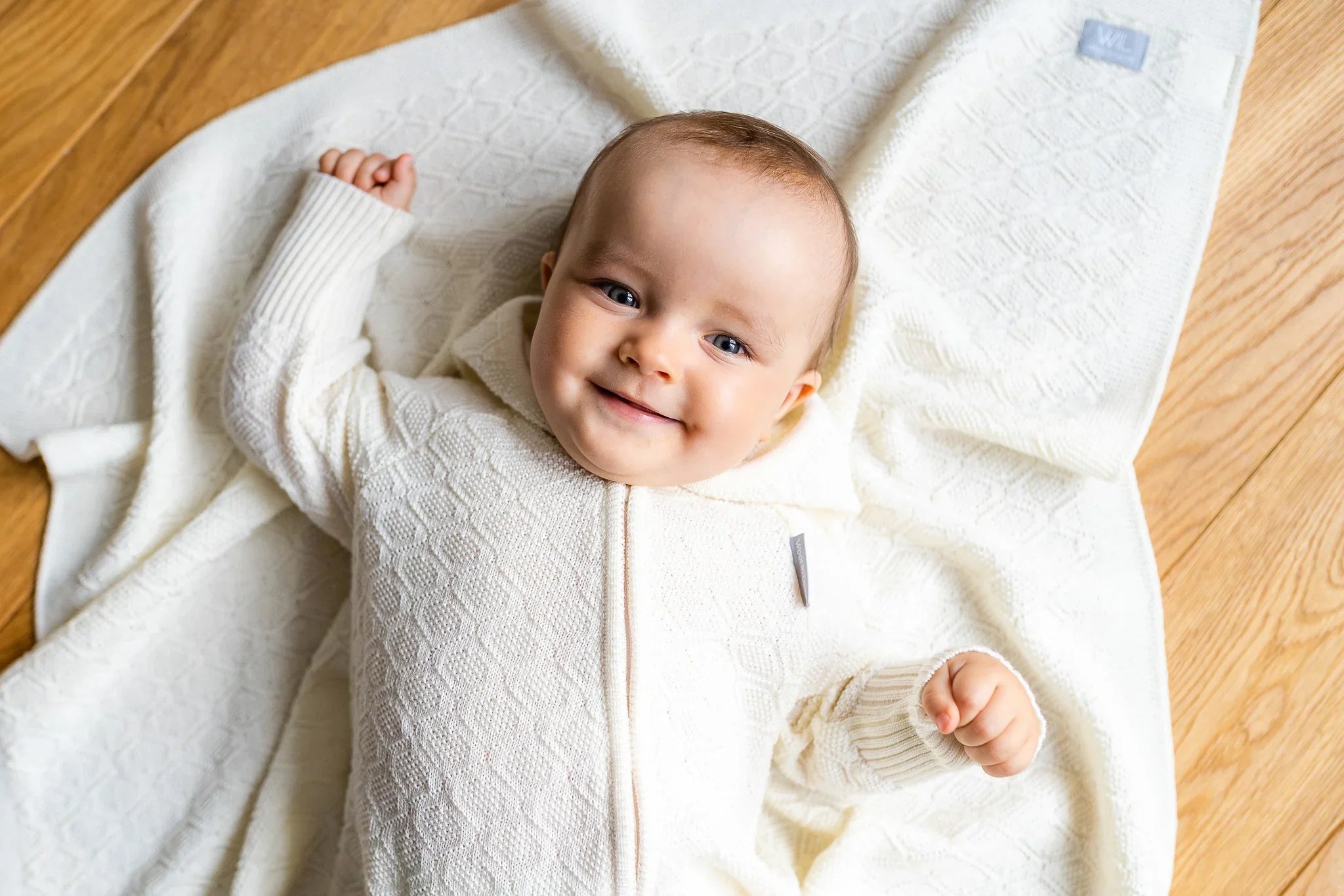 Bébé souriant en grenouillère tricotée crème sur une couverture assortie à motif losanges