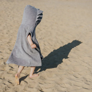 Enfant portant un poncho de bain gris à capuche avec détail nageoire sur une plage de sable