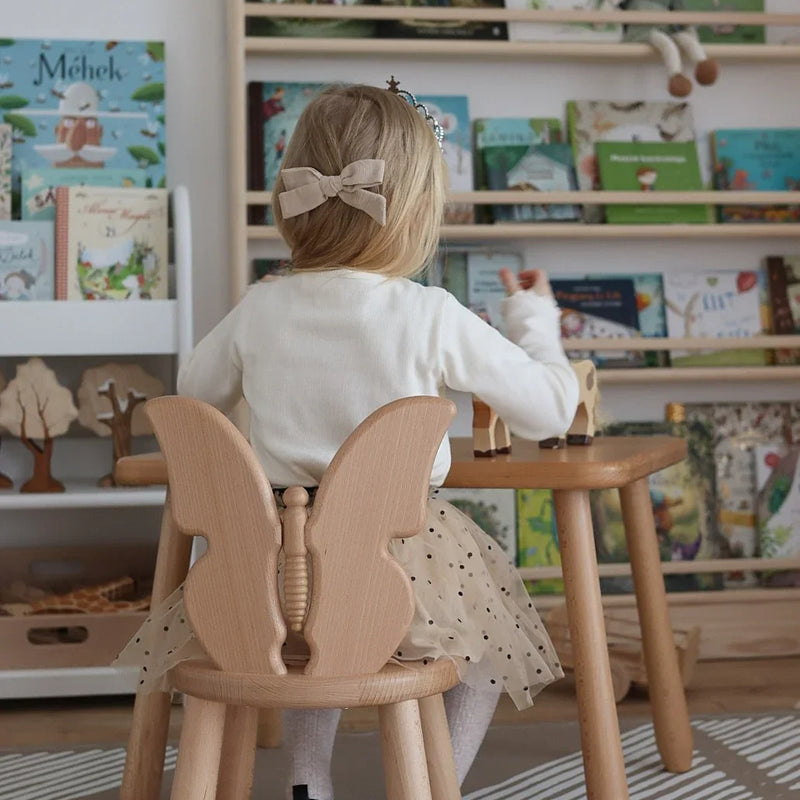 Silla infantil con respaldo de mariposa y mesa a juego de madera, acabado natural, en habitación infantil con estantería