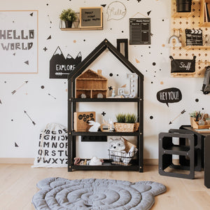 Black house-shaped kids shelf styled with baskets, books and toys in a monochrome playroom