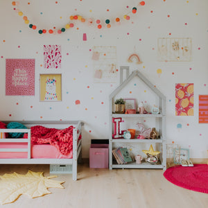 Grey house-shaped shelf beside a pink children’s bed in a colourful bedroom with wall art