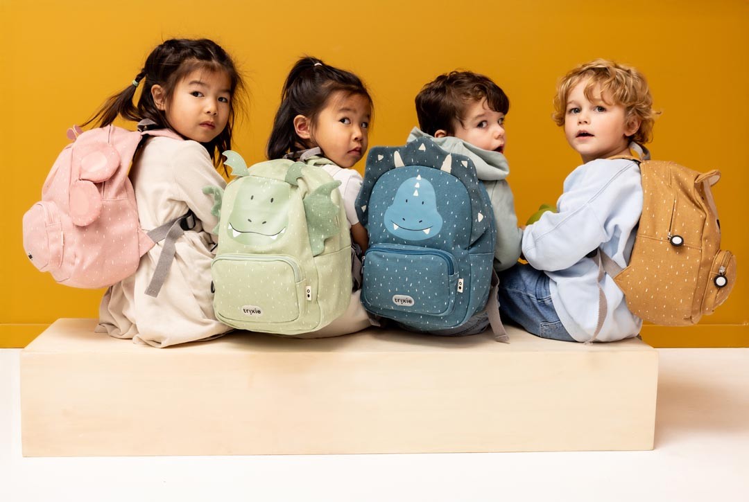 Four children wearing pink, green, blue and brown Trixie animal backpacks against a warm yellow background