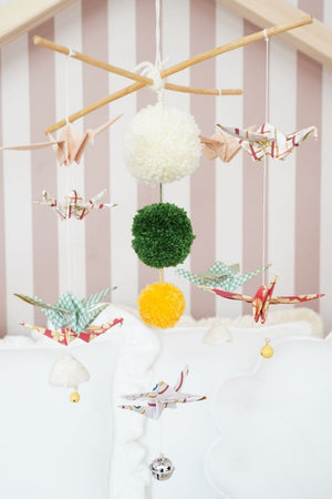 Full view of the Vintage Vibe nursery mobile with paper birds, cream, green and yellow pompoms and tiny bells