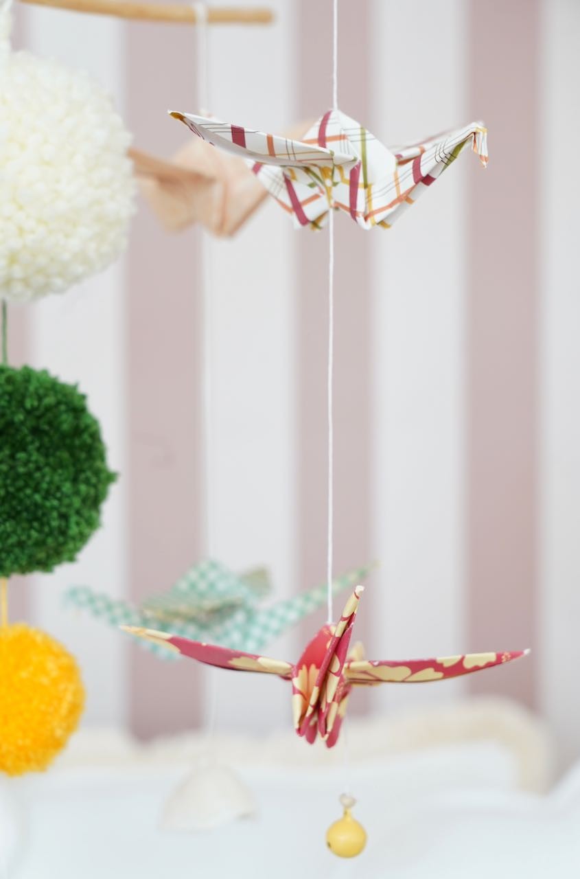 Close-up of patterned origami cranes and a yellow bell on the Moi Mili Vintage Vibe mobile