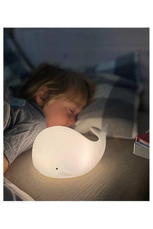 Veilleuse baleine en silicone blanc sur une table de chevet, diffusant une douce lueur dans la chambre