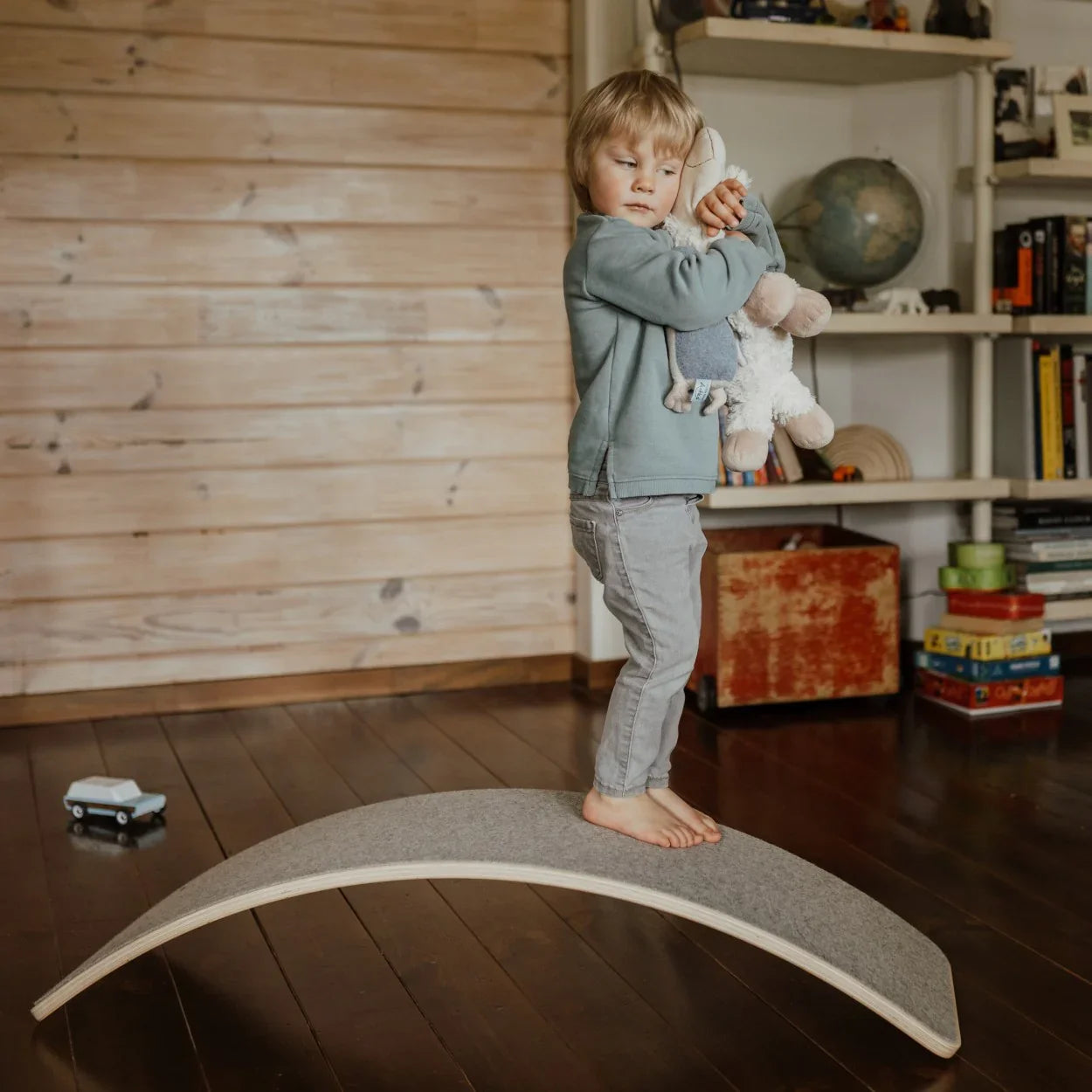 Child standing barefoot on gray felt balance board with wooden edges in nursery