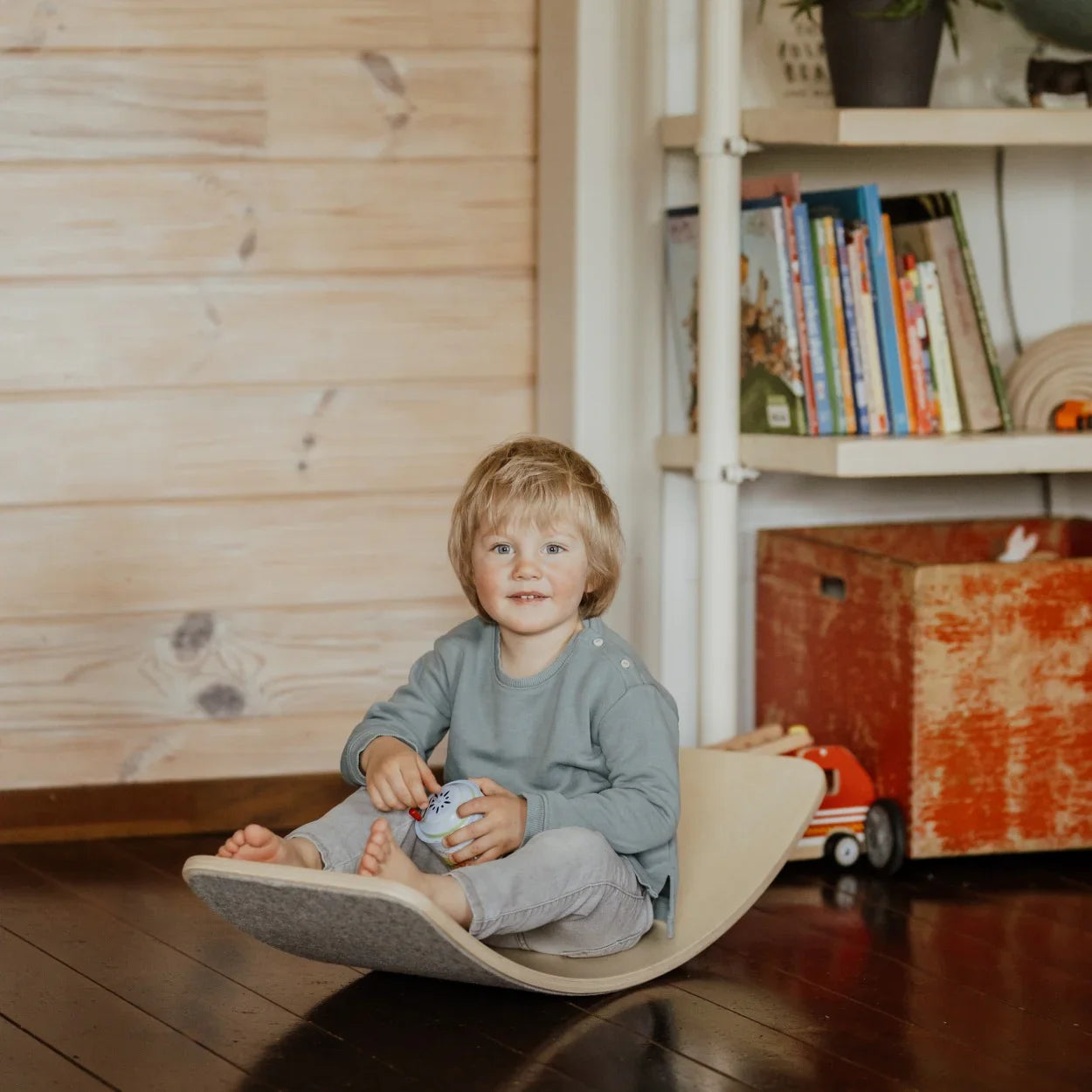 Child on wooden rocking toy with gray felt seat, nursery playroom setting