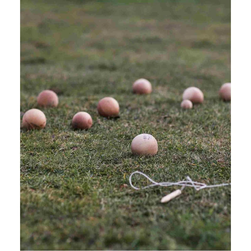 Wooden ball toss game arranged on grass with natural wooden balls and rope marker, designed for outdoor screen-free play and coordination skills.