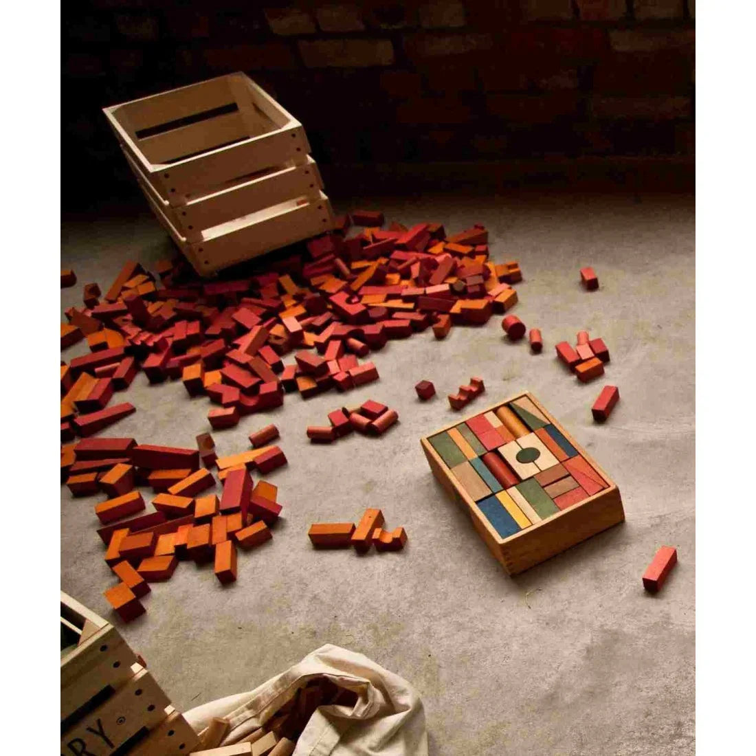 Wooden Story building blocks in warm red and orange tones spread across the floor with wooden storage boxes