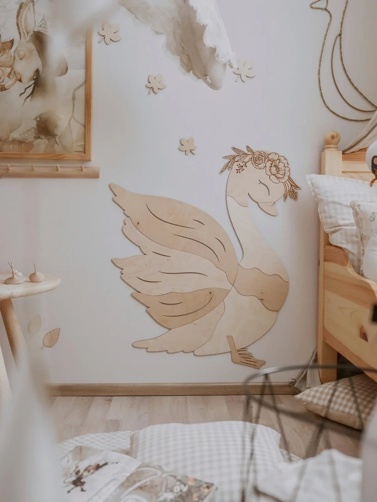 Decorazione da parete in legno a forma di cigno con corona floreale in un contesto di arredamento neutro per nursery
