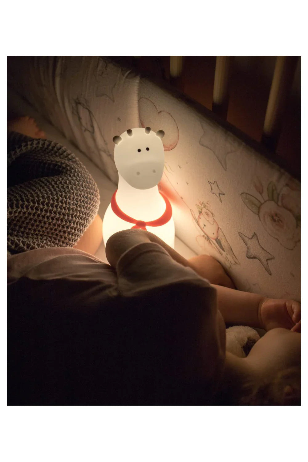 Veilleuse girafe en silicone brillant près d'un enfant endormi dans un lit à motifs étoiles